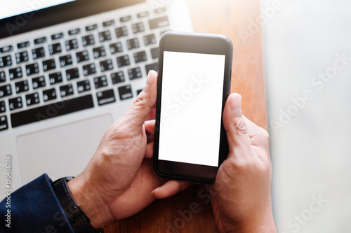 Mockup image of a man's hand holding white mobile phone with blank black desktop screen on thigh in cafe