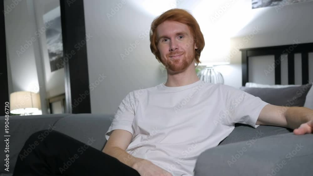 Thumbs Up by Redhead Man Sitting on Couch in Bedroom Thumbs Up by Redhead Man Sitting on Couch in Bedroom