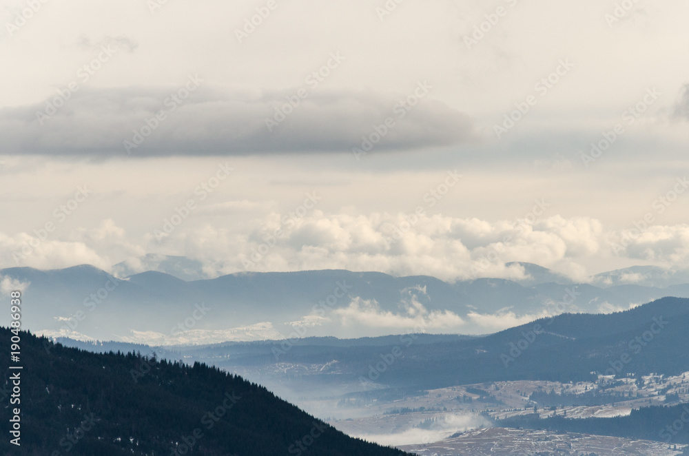 Winter in the mountains, the clouds lie above the tops of the mountains, snow on the peaks