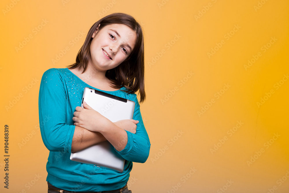 Girl holding a digital tablet in hands on yellow background in studio Girl holding a digital tablet in hands on yellow background in studio