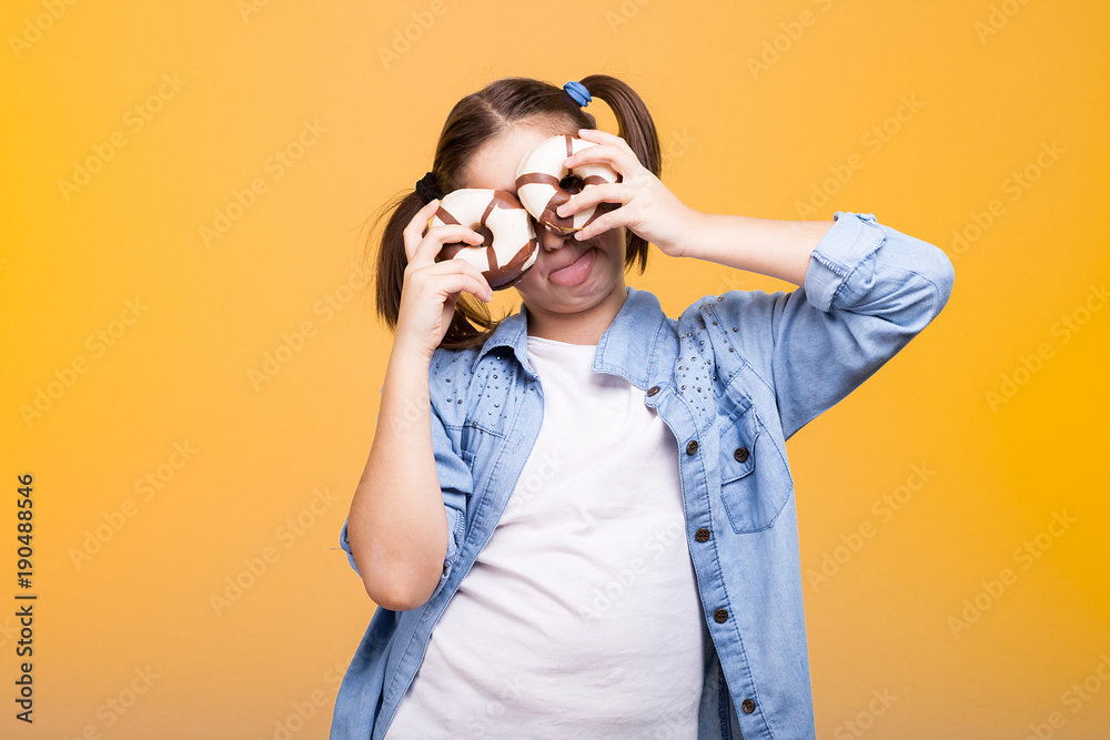 Cute girl in studio playing with two donuts on yellow background Cute girl in studio playing with two donuts on yellow background