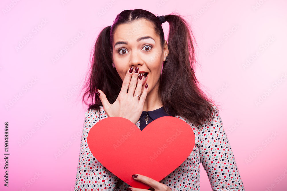 Surprised Woman with a red papper heart in hands on pink background Surprised Woman with a red papper heart in hands on pink background
