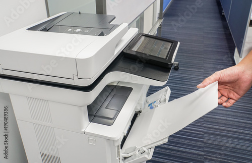 close up businessman hand put blank paper sheet into printer input for copying and scanning documents photo