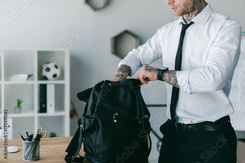 cropped shot of young tattooed businessman opening backpack at workplace