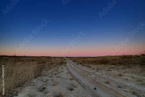 Rural road in the countryside after the sunset. Traveling during the twilight.
