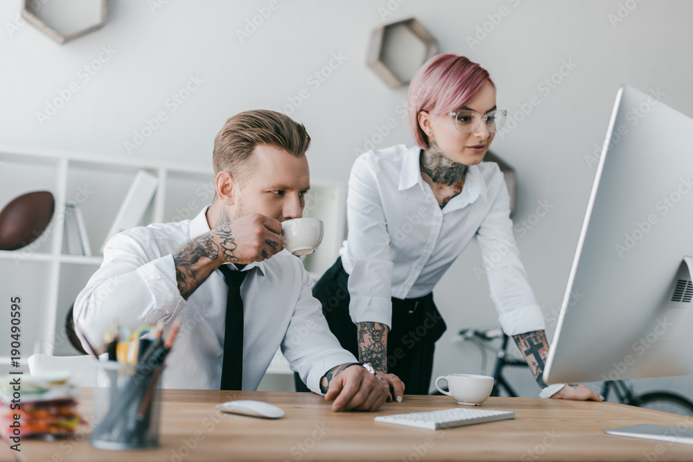 young tattooed business people using desktop computer together young tattooed business people using desktop computer together
