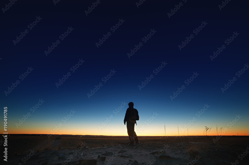 A tourist on the road against the background of a bright sunset and a cloudless sky.