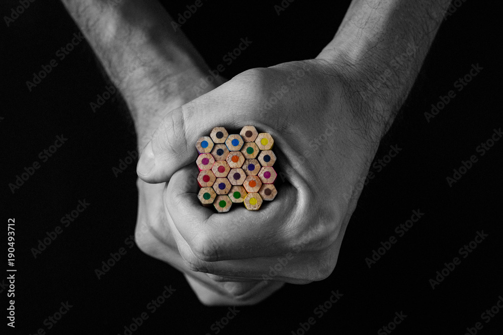 Colored pencils in hand on a black background. Creative concept. Black and white image Colored pencils in hand on a black background. Creative concept. Black and white image
