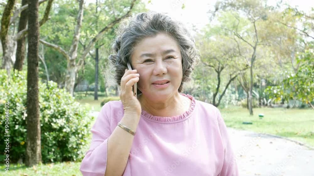 Asian couple elder people relax at park. Elder woman using smartphone with happy emotion. People lifestyle concept Asian couple elder people relax at park. Elder woman using smartphone with happy emotion. People lifestyle concept