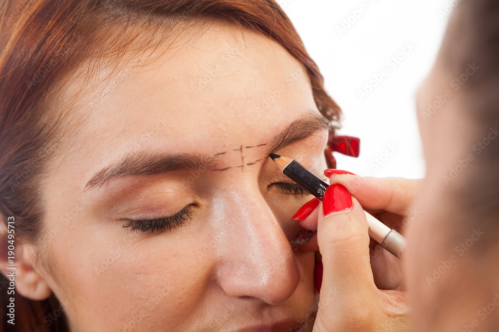 Close-up of an eyebrow brushes a perfect eyebrow shape with a black pencil young red-haired woman on a white isolated background, front view