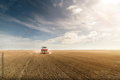 Farmer with tractor seeding - sowing crops at agricultural fields