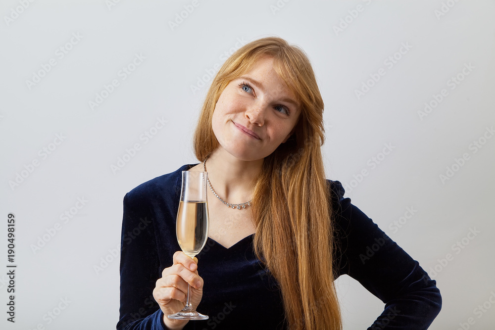 Studio headshot of young elegant lady with red hair and freckles dressed in dark velvet holding a glass of champagne and playfully looking aside. Party flirting concept. Studio headshot of young elegant lady with red hair and freckles dressed in dark velvet holding a glass of champagne and playfully looking aside. Party flirting concept.