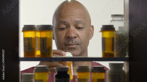 Man reading label of pill bottle in medicine cabinet, wide shot