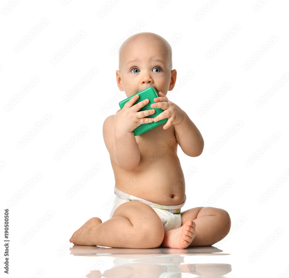 Infant child baby boy toddler sitting naked in diaper with green brick toy looking up Infant child baby boy toddler sitting naked in diaper with green brick toy looking up