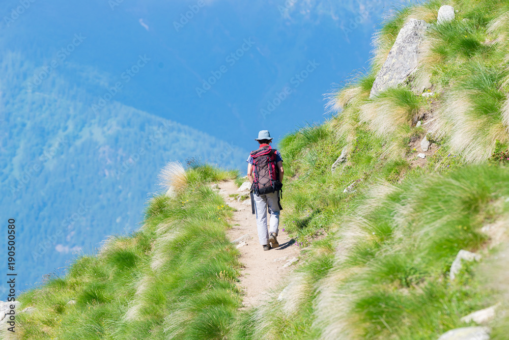 Backpacker walking on hiking trail in the mountain. Summer adventures summer vacation on the Alps. Wanderlust people traveling concept.