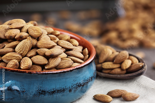 Whole almonds in bowl and wooden spoon against a rustic background.