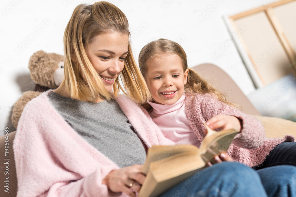 happy mother and daughter reading book together on sofa happy mother and daughter reading book together on sofa