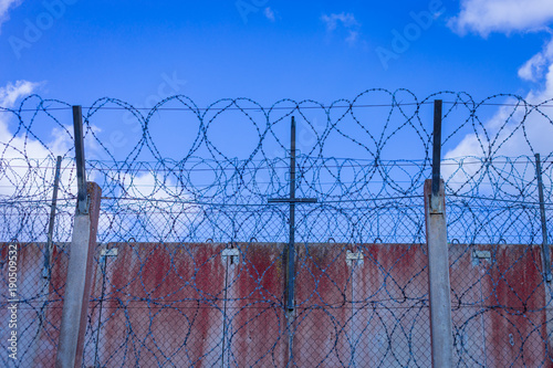 Roll of razor wire on concrete wall. Barbed wire on the wall. Prison wall against blue sky