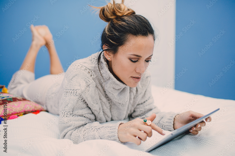 Young beautiful woman reading tablet at home lying on bed.