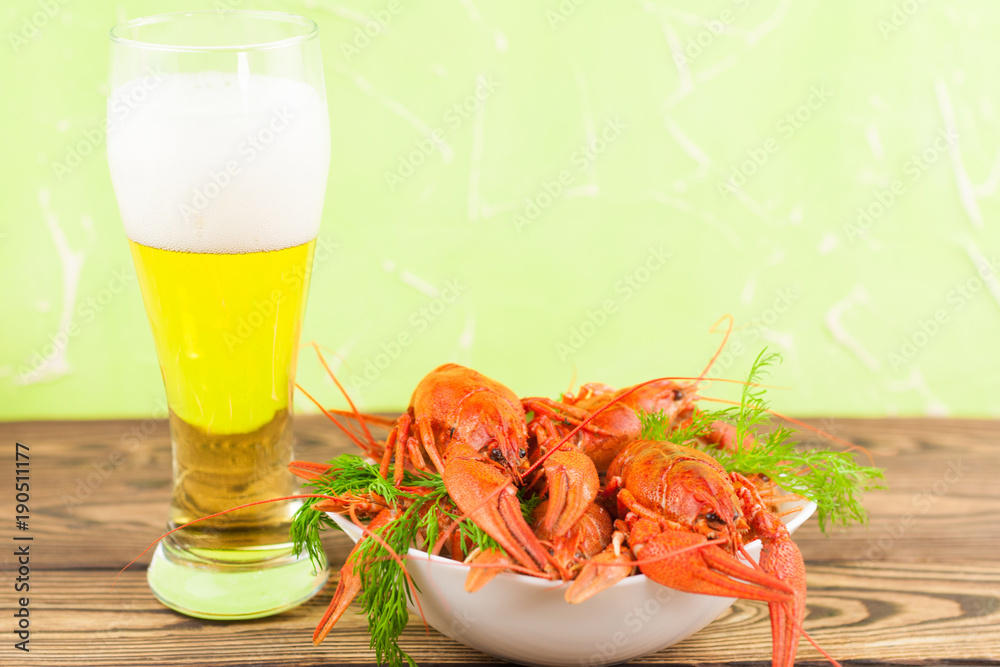 Heap of red boiled crayfish with fresh dill in white ceramic bowl near full glass of beer with foam on old brown rustic table Heap of red boiled crayfish with fresh dill in white ceramic bowl near full glass of beer with foam on old brown rustic table