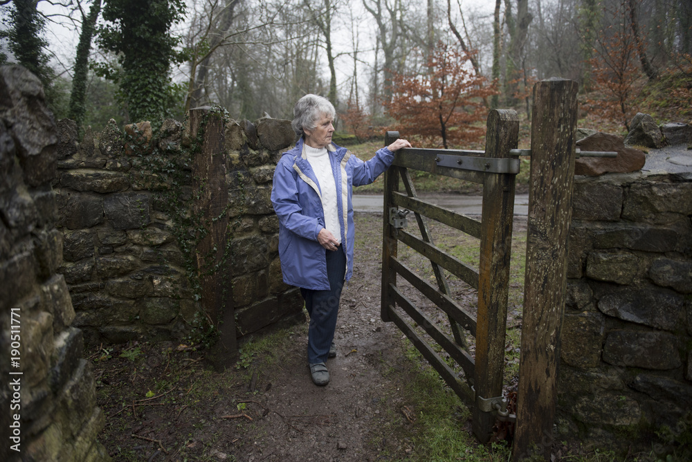 Senior woman walking through a farm gate on a rainy day in winter Senior woman walking through a farm gate on a rainy day in winter