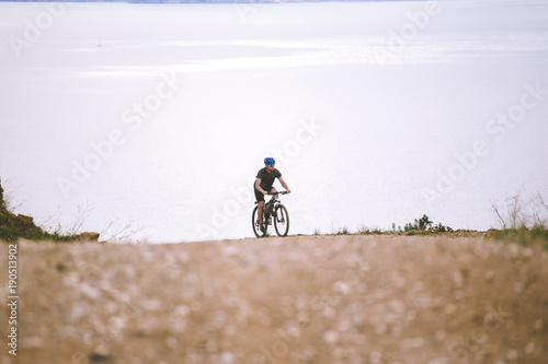 Theme tourism and cycling on mountain biking. guy rides uphill on a rocky, rocky road against the background of the Mediterranean Sea in Spain on the shore of the kosta brava in helmet and sportswear