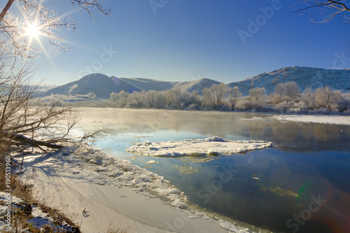 Bright sun in the cloudless sky. Freezing river from the hilly banks and large ice floes.