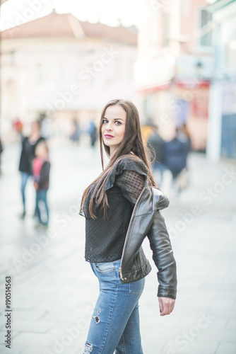 Modern attractive woman standing on a street close up portrait, woman touching hair, behind her are passers-by on the street, she enjoys life © Amir Bajric