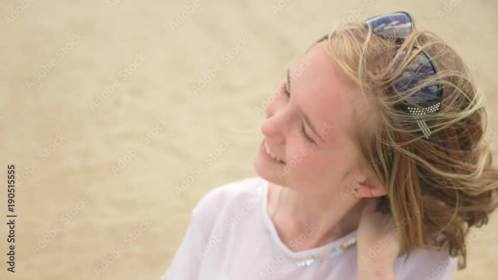 Close up portrait of beautiful young woman teenager. Hair blowing in wind on beach in slow motion. She is smiling and attractive. On her head are sunglasses.
