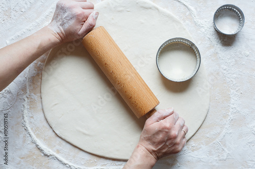 The process of making homemade traditional dumplings. Rolling out dough. Woman's hands. Pierogi, pelmieni, ravioli. Rolling pin, mould, dough. White background with flour. Top view.