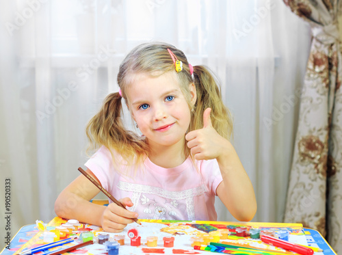 Девочка со светлыми волосами сидит за столом и рисует красками картину по номерам. Картина по номерам.