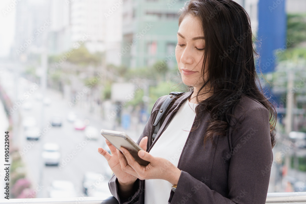 middle aged asian woman checking appointment with client in mobile application while walking in the city to go to meeting.