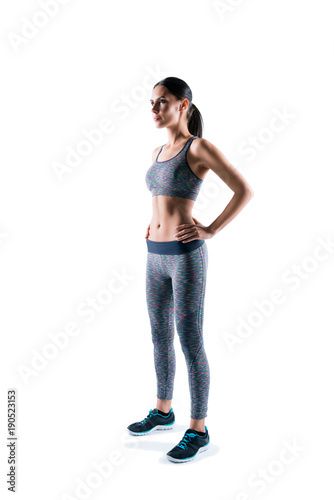 Vertical full-size full-length half-turned portrait of slim sportive beautiful sexy young attractive sport woman, she is staying still against white background