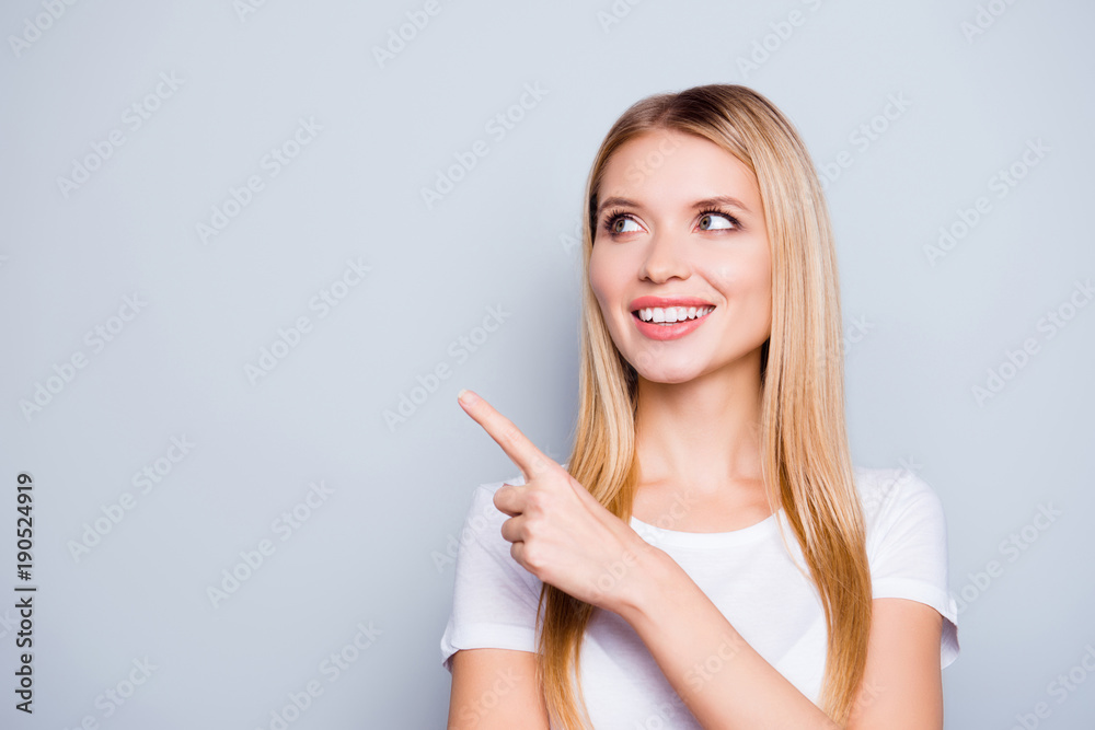 Close up portrait of happy excited beautiful lovely cute woman with perfect skin, she is showing on a copy space near her shoulder and looking aside, isolated on grey background Close up portrait of happy excited beautiful lovely cute woman with perfect skin, she is showing on a copy space near her shoulder and looking aside, isolated on grey background