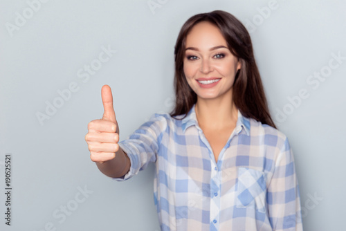 Portrait of gorgeous  cute  cheerful  attarctive woman showing  thumb up in checkered shirt over grey background