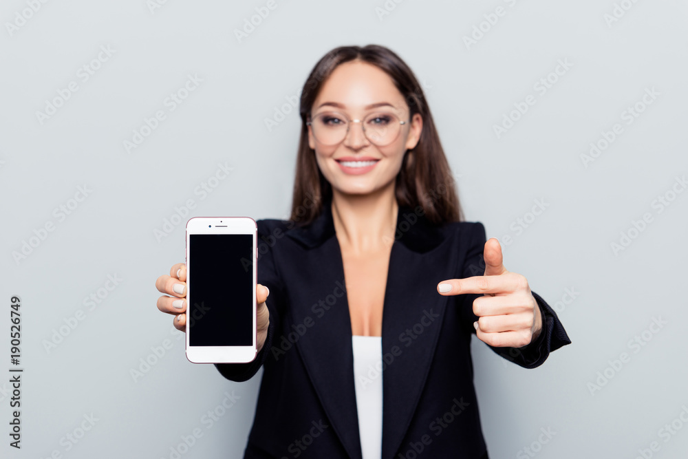 Portrait with copy space of pretty, charming, nice woman recommend to do online shopping using smartbphone, presenting, indicating on brand new mobile phone over grey background