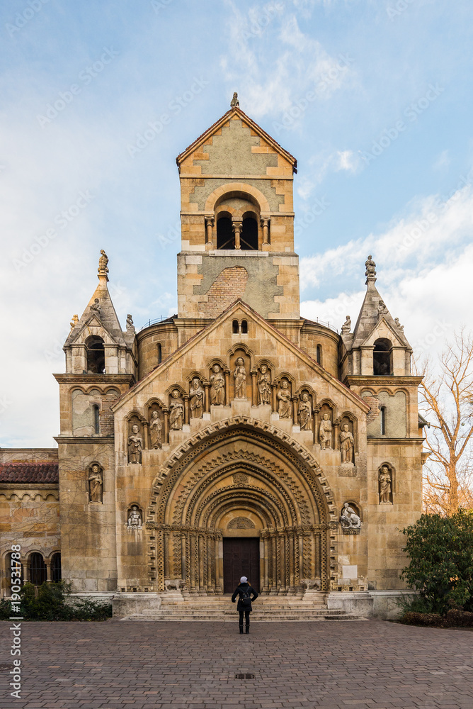 Young woman is standing in front of The Chapel of Jak in Vajdahunyad Castle in the City Park in Budapest, Hungary.