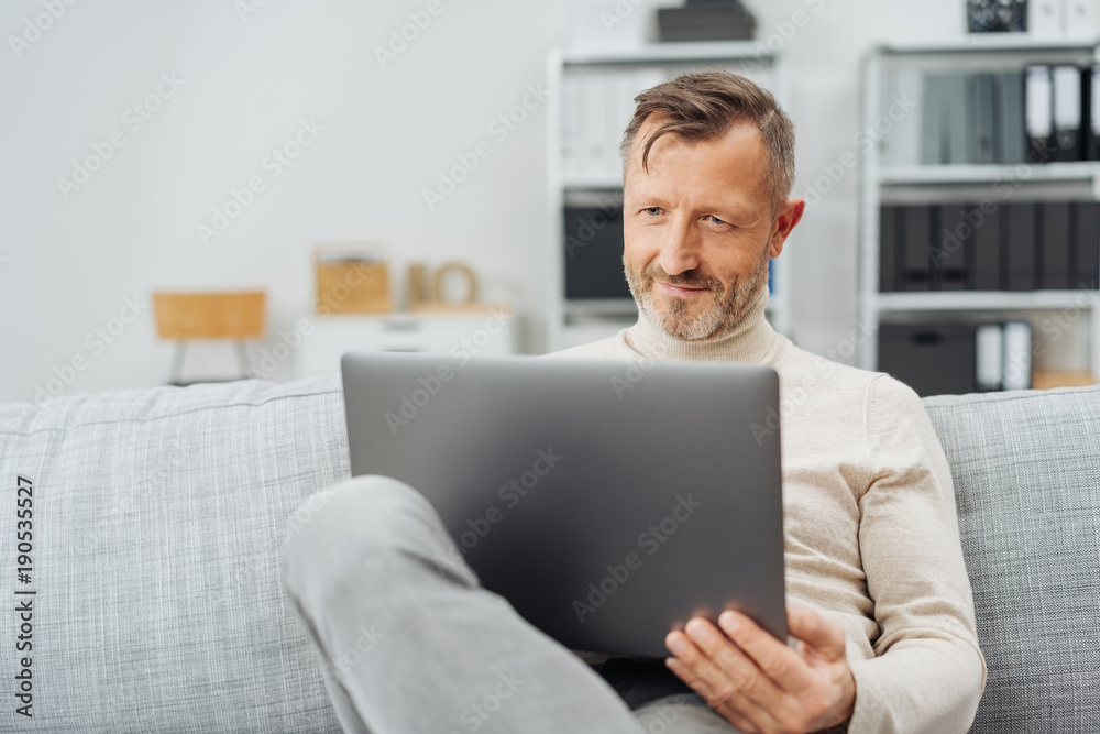 Man sitting using a laptop with a pleased smile Man sitting using a laptop with a pleased smile