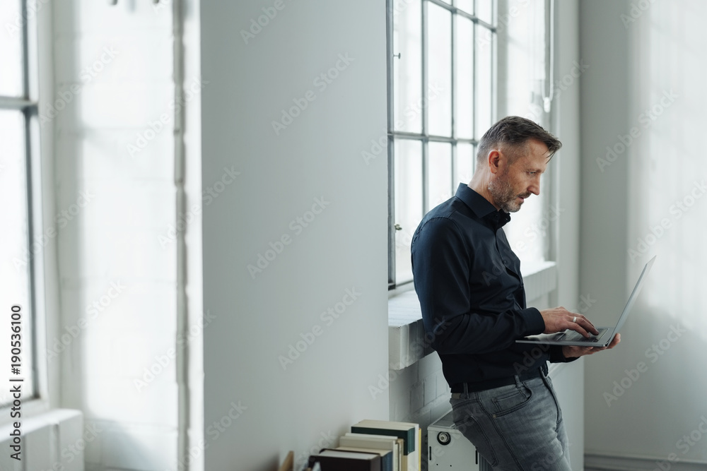 Man sitting perched on a radiator using a laptop