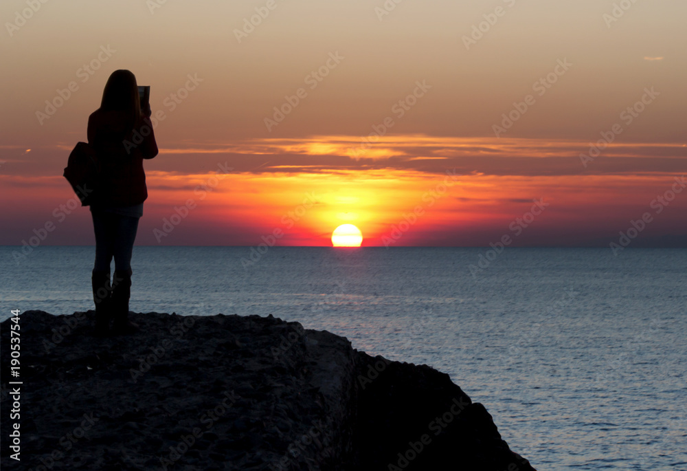 Silhouette portrait of female watching and take a photo with beautiful sunset at the sea background, Sea & sunset over sea horizon landscape in nature background.
