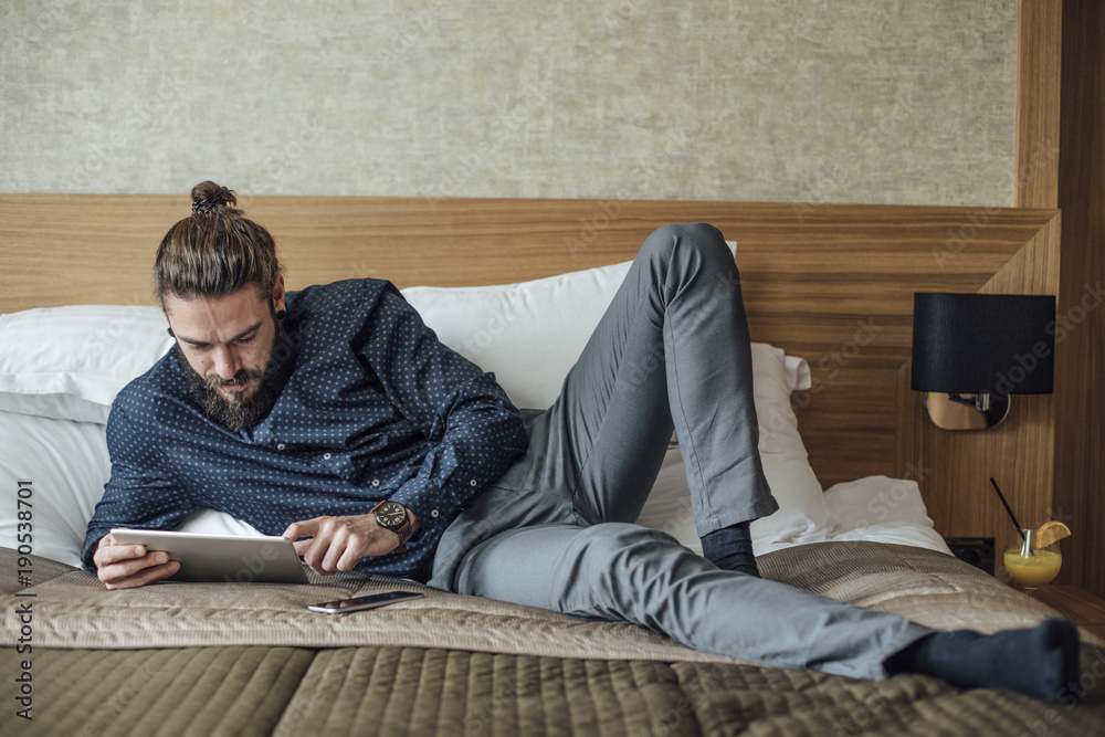 Man Lying on Bed and Reading on Tablet
