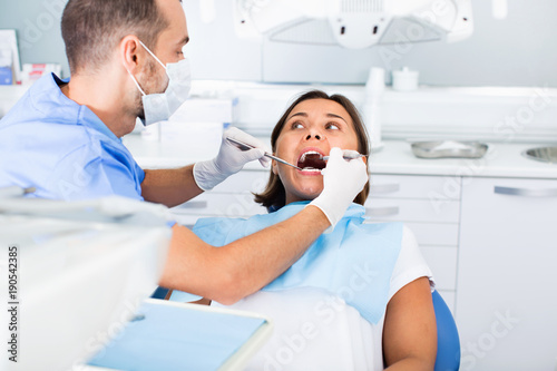 Dentist is treating woman patient which is sitting in dental chair