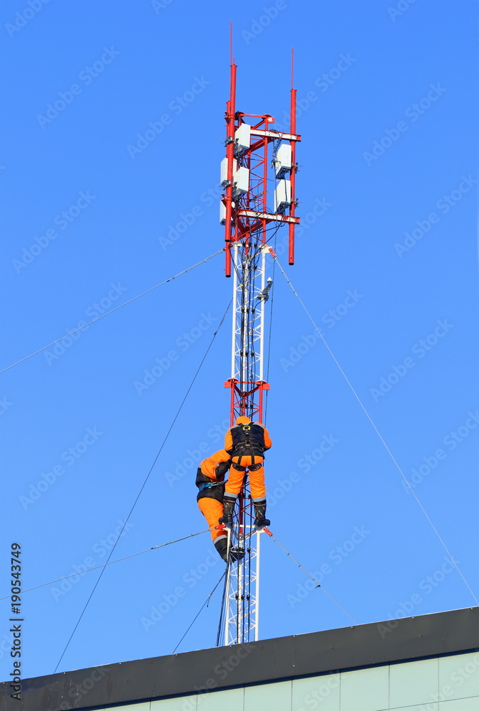 Base station of cellular communication and working installers on the background of blue sky Base station of cellular communication and working installers on the background of blue sky