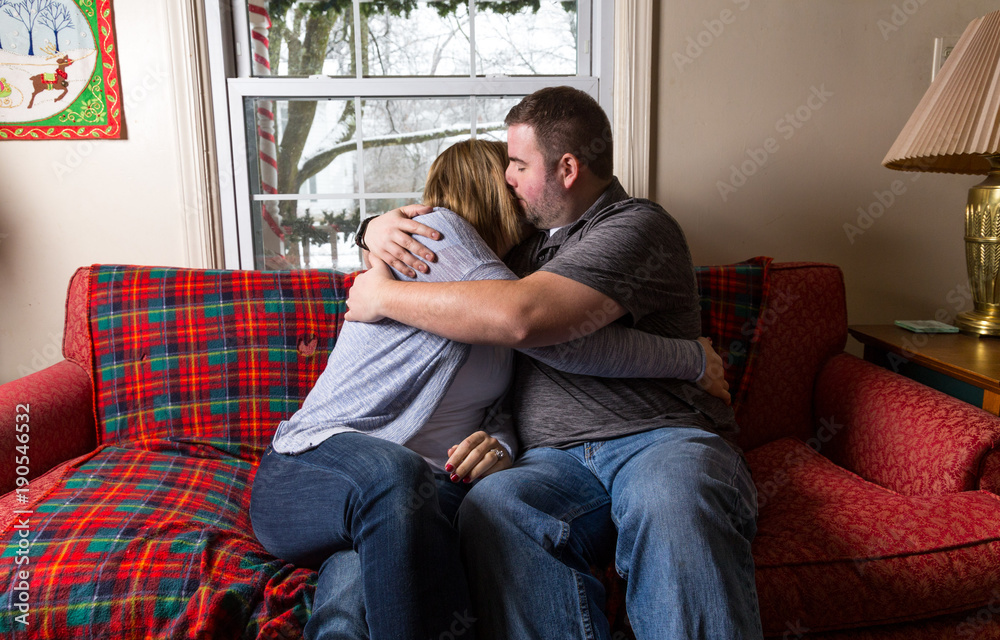 A Young Caucasian Couple Excitedly Waits And Prays For Good News As They Sit On Their Living Room Couch. A Young Caucasian Couple Excitedly Waits And Prays For Good News As They Sit On Their Living Room Couch.
