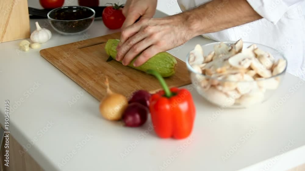Side view of cook taking a squash from the table and starting to cut it Side view of cook taking a squash from the table and starting to cut it