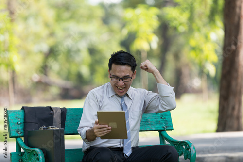 Young businessman looking at digital tablet in the park. He showing signs of rejoicing at their success. A successful businessman concept