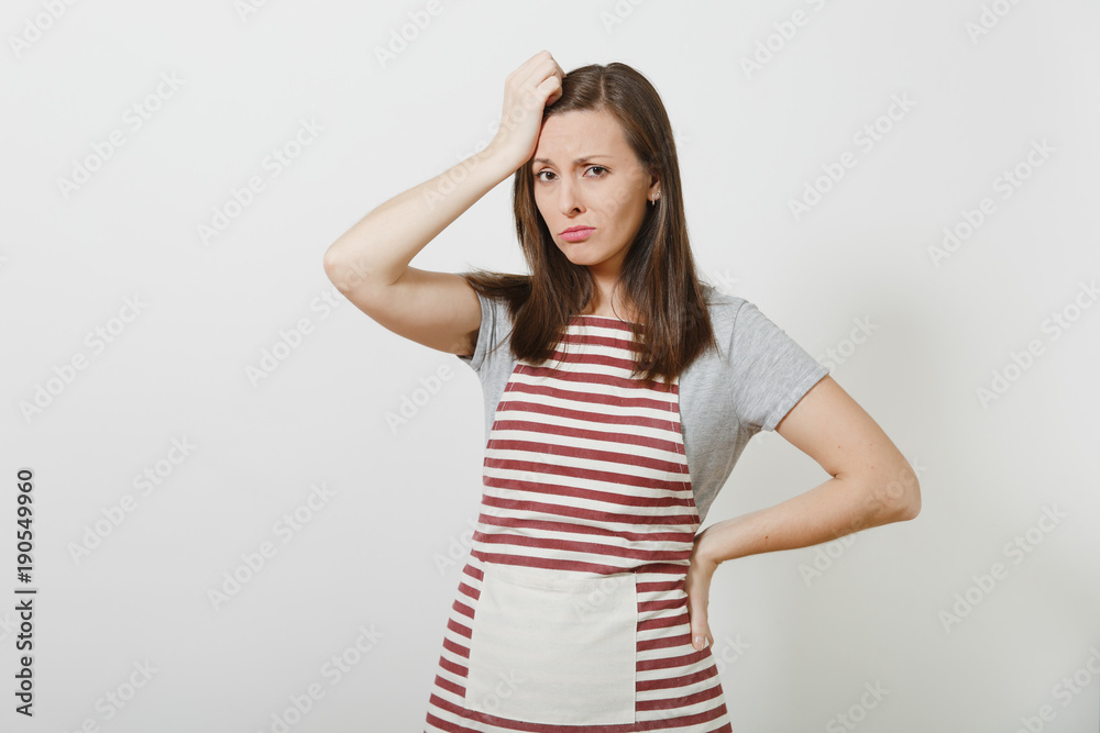 Young attractive sad upset tired brunette caucasian housewife in striped apron isolated on white background. Beautiful housekeeper woman put and touch her hand to head. Copy space for advertisement. Young attractive sad upset tired brunette caucasian housewife in striped apron isolated on white background. Beautiful housekeeper woman put and touch her hand to head. Copy space for advertisement.