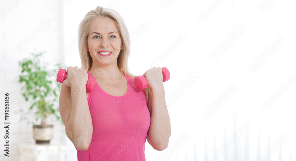 Happy middle aged woman lifting dumbbells at home in the living room Happy middle aged woman lifting dumbbells at home in the living room