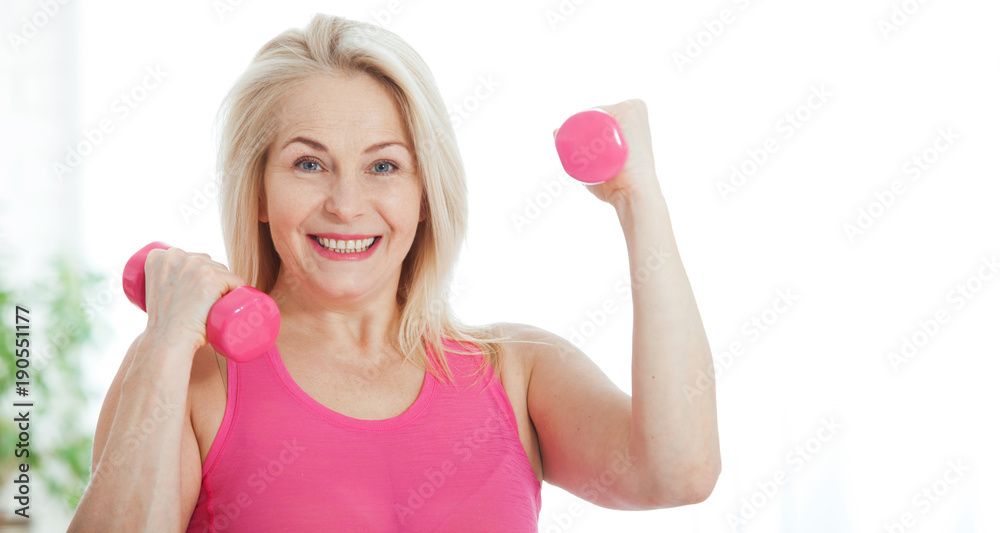 Happy middle aged woman lifting dumbbells at home in the living room Happy middle aged woman lifting dumbbells at home in the living room