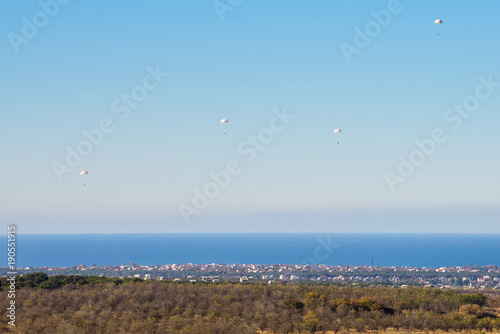Airborne troops a mass parachute drop over the sea. On a blue sky background.